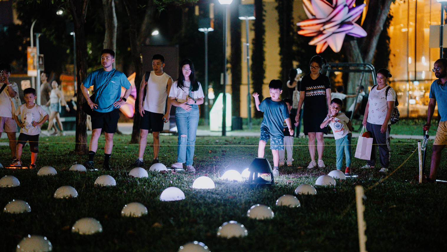 People at night art installation with lights on grass.